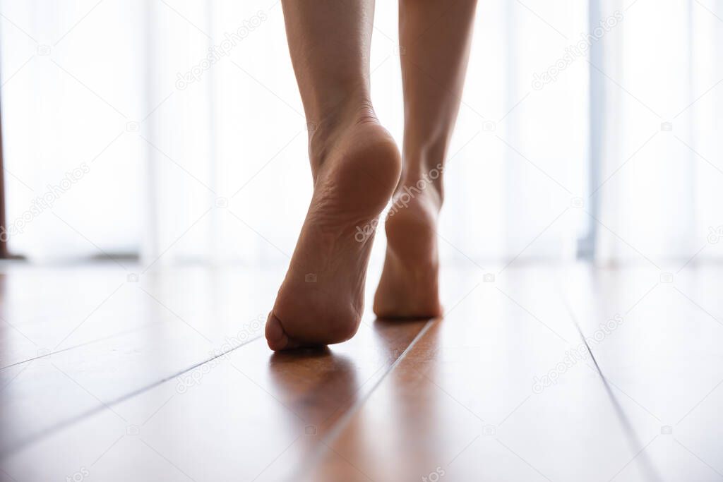 Female feet walks on warm laminate floor closeup rear view
