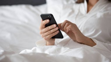 Akıllı telefonuyla yatakta uzanan kadın sosyal ağların mesajlarını kontrol ediyor