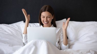 Sabahları dizüstü bilgisayarla yatakta oturan kadın mutlu olur.