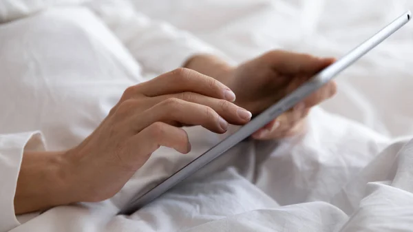 Primer plano manos femeninas sosteniendo tableta navegar por Internet acostado en la cama — Foto de Stock