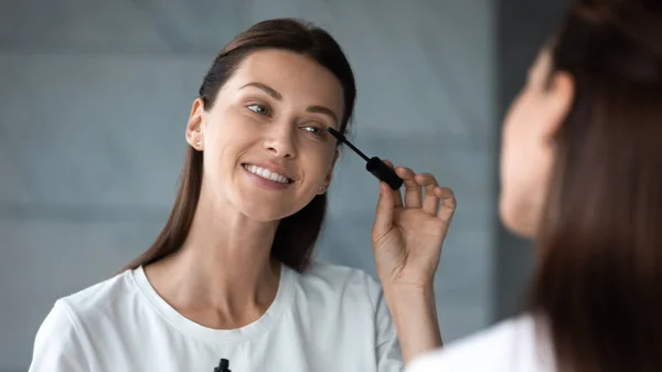 Mujer aplicando rímel, cara femenina reflejada en el espejo —  Fotos de Stock