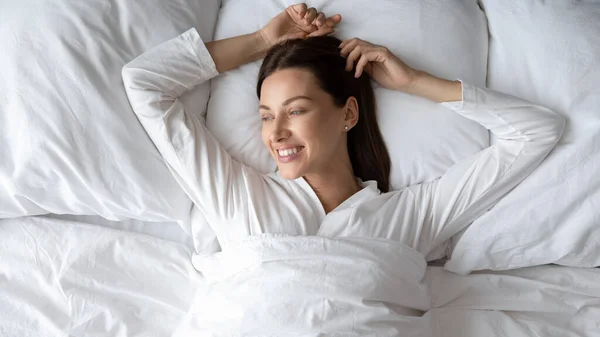Milenial mujer en pijama blanco acostado en la cama se siente descansado —  Fotos de Stock
