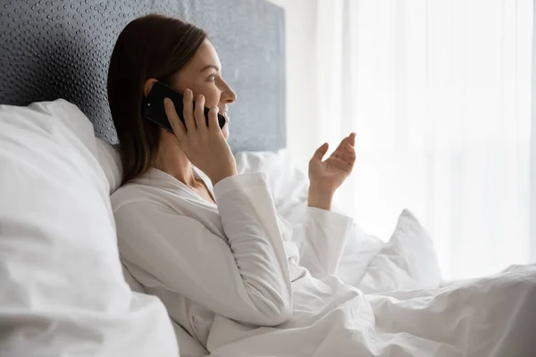 Descansada mujer despierta sentada en la cama hablando por teléfono — Foto de Stock