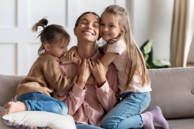 Mutlu genç anne, küçük kızlarıyla hassas bir anın tadını çıkarıyor.