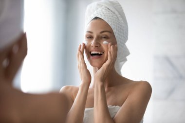 Kadın yüzüne dokunmak cildine dikkat etmek için nemlendirici krem kullanıyor.