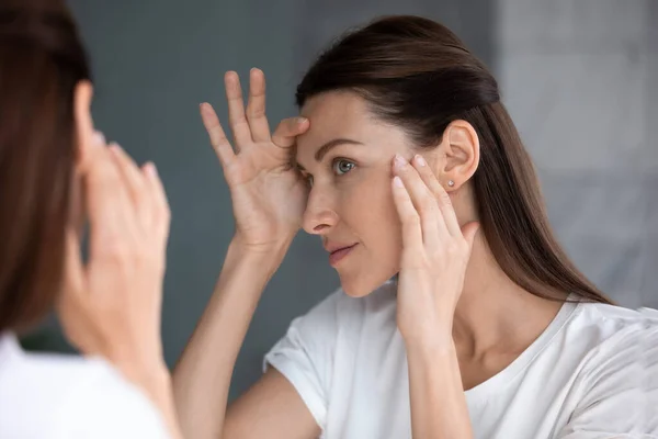 Satisfied woman looking in mirror check face after beauty treatment — Stock Photo, Image