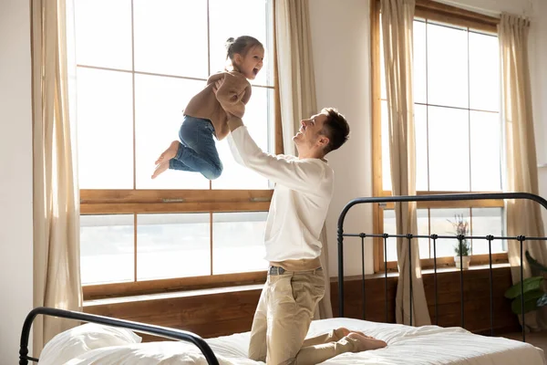 Happy father playing with little daughter, jumping on bed