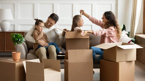 Genitori felici che giocano con i bambini il giorno del trasloco, disimballando scatole — Foto Stock