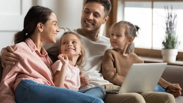 Evde dizüstü bilgisayar kullanan iki küçük kızı olan mutlu ebeveynler. — Stok fotoğraf