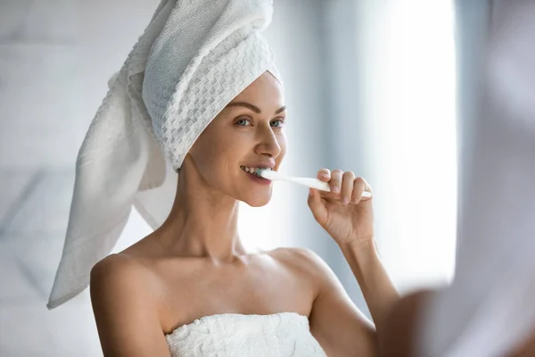 Pretty woman reflected in mirror brushing teeth feels satisfied