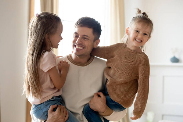 Смеющийся отец держит в руках двух очаровательных маленьких дочерей
