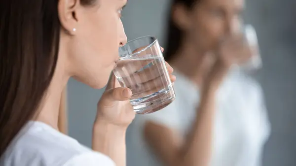 Mulher refletindo no espelho em pé dentro de casa bebendo água filtrada closeup — Fotografia de Stock