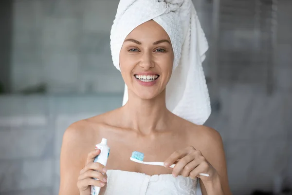 Beautiful woman holding toothpaste and toothbrush smiles looks at camera — Stock Photo, Image