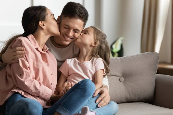 Mother and little daughter kissing father on cheek