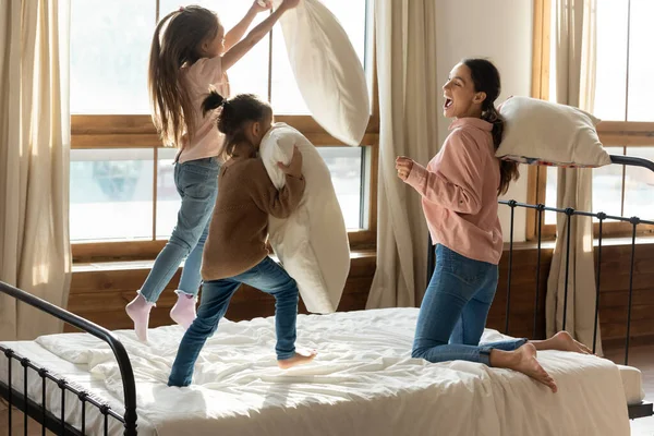 Feliz madre jugando almohada lucha con dos hijas pequeñas — Foto de Stock