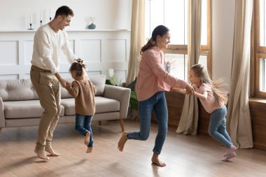 Mutlu ebeveynler küçük kızlarıyla oturma odasında dans ediyor.