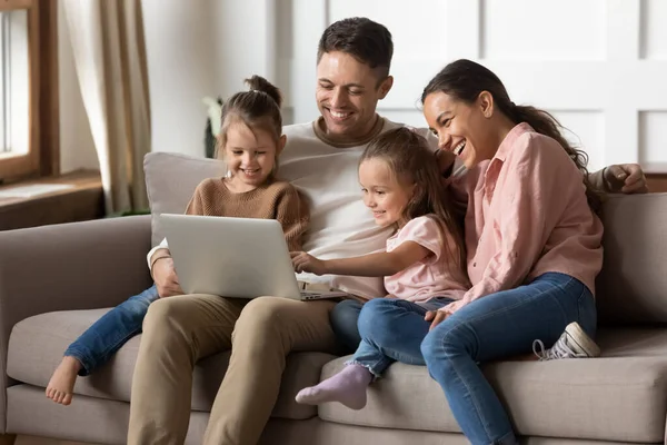 Счастливая семья с двумя маленькими дочерьми, которые вместе пользуются ноутбуком — стоковое фото