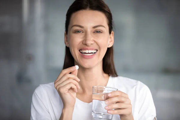 Cheerful woman holding pill glass of water looking at camera — Stock Photo, Image