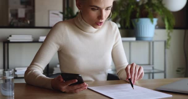 Trabajadora joven de negocios enfocada usando papel de chequeo de teléfonos inteligentes — Vídeos de Stock