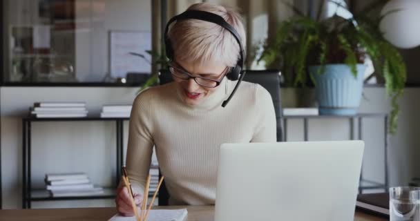Улыбающаяся деловая женщина в наушниках звонит на ноутбук — стоковое видео