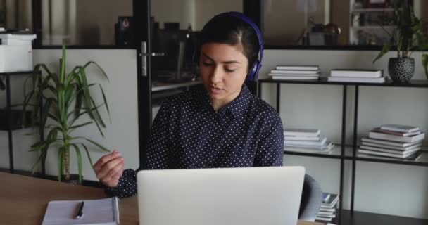 Poważny tysiącletni indyjski menedżer nosi słuchawki wideo rozmowy na laptopie — Wideo stockowe