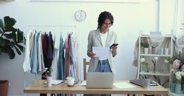 Smiling young female fashion designer using smart phone at workplace — Stock Video