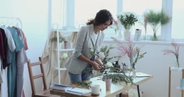 Gülümseyen genç tasarımcı çiçekçi yaratıcı stüdyoda çiçek düzenliyor.