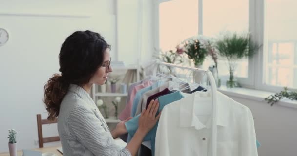 Lächelnder Modeschöpfer prüft neue Kollektion, die an Regalen hängt — Stockvideo