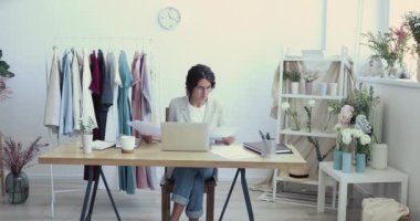 İş yerinde dizüstü bilgisayar kullanan genç moda tasarımcısı raporları analiz ediyor