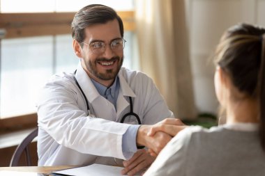 Toplantıda gülümseyen erkek doktor, el sıkışan kadın hasta.