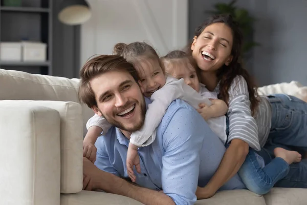 Überglückliche junge Eltern entspannen mit kleinen Töchtern auf dem Sofa — Stockfoto