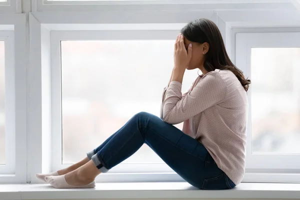 Mulher deprimida sentada no peitoril da janela chorando rosto coberto com palmas — Fotografia de Stock