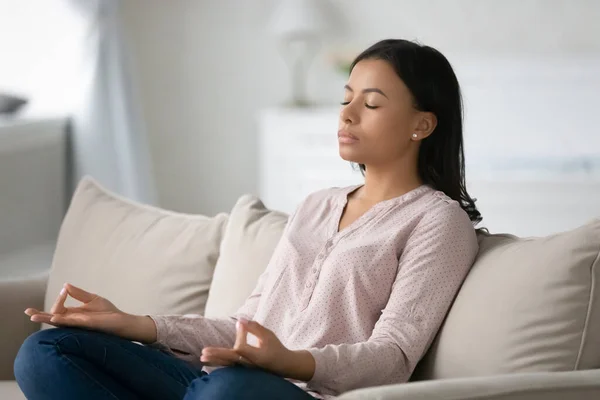 African girl seated cross-legged on couch do meditation practice — Stock Photo, Image