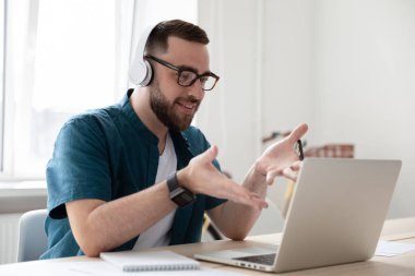 Kulaklıklı gülümseyen işadamı dizüstü bilgisayara bakıyor ve Webinar izliyor..
