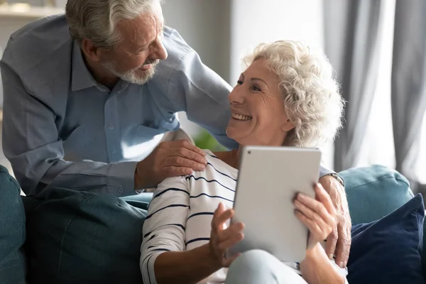 Sonriendo mujer madura utilizando la tableta de computadora digital, charlando con el marido . — Foto de Stock