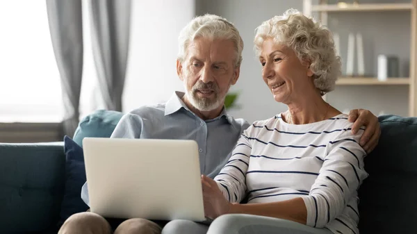 Glad medelålders familj par avkopplande på soffan, med hjälp av dator. — Stockfoto