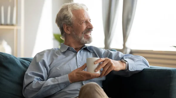 Счастливый пожилой человек отдыхает на диване с чашкой чая . — стоковое фото