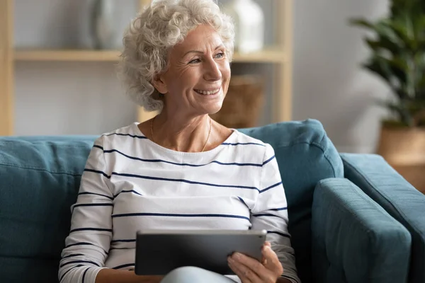 Dreamy pleasant middle aged woman using computer digital tablet.