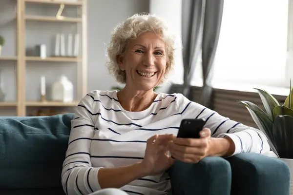 Sorrindo positivo mulher de meia idade segurando smartphone em mãos . — Fotografia de Stock