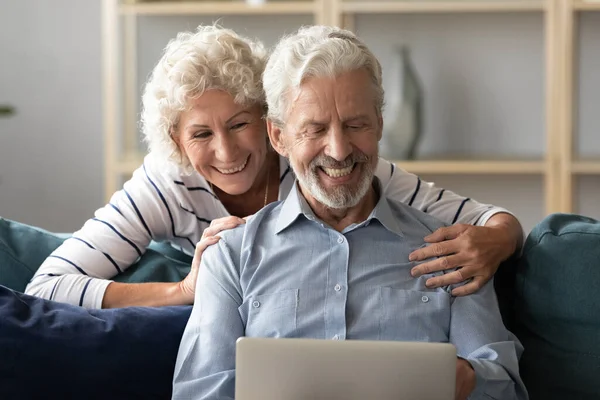 Feliz pareja de ancianos disfrutando de usar el ordenador portátil en casa . — Foto de Stock