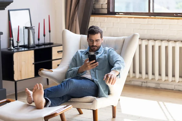 Millennial hombre relajarse en la silla utilizando el dispositivo de teléfono celular — Foto de Stock