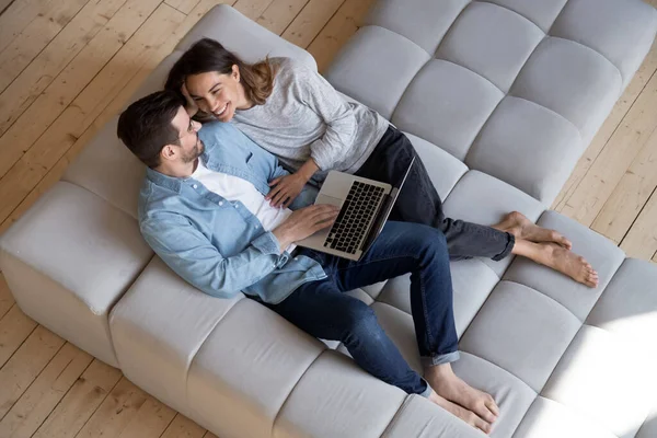 Feliz pareja milenaria relajarse en el sofá utilizando el ordenador portátil en casa —  Fotos de Stock