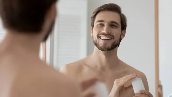 Smiling young man use facial balm or cream in bathroom — Stock Photo, Image