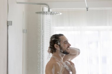 Çıplak genç adam banyoda duş alıyor.