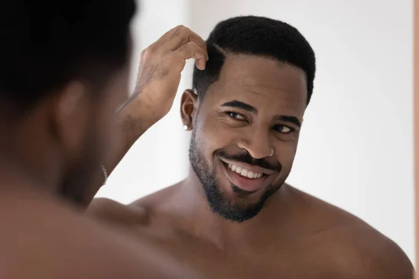 Sonriente hombre afroamericano mirada en el espejo en el baño — Foto de Stock