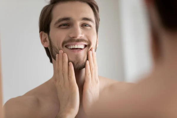 Smiling Caucasian man look in mirror touching face — Stock Photo, Image