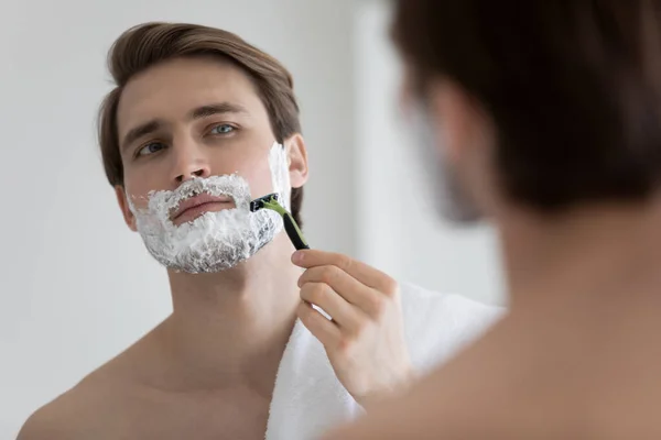 Caucasian man look in bat mirror shaving in morning — Stock Photo, Image