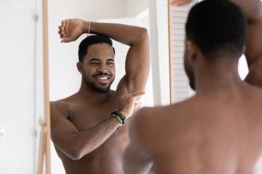 Çıplak Afrikalı Amerikalı adam banyoda deodorant kullanıyor.