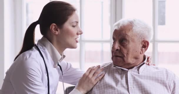 Молодая медсестра обнимает за плечи улыбающегося старого пациента на пенсии . — стоковое видео