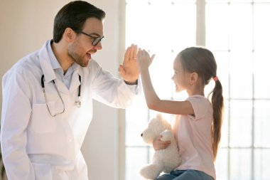 Gülümseyen küçük kız hastanede erkek doktorla selamlaşıyor.